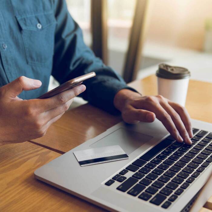 Client sitting at desk holding his phone with a financial card on his laptop