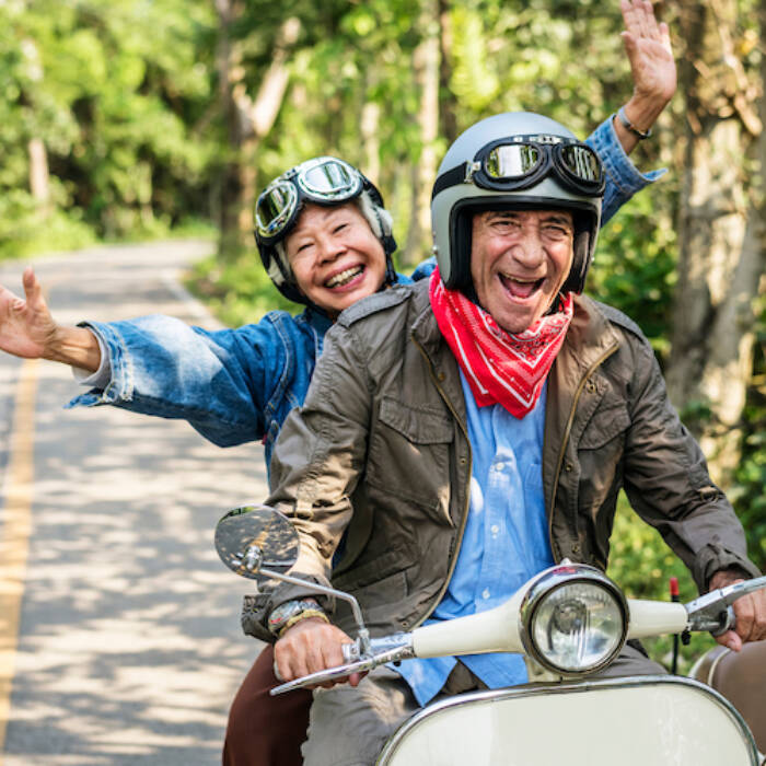 Retired elderly senior couple outside riding a motorcycle together smiling happily enjoying retirement