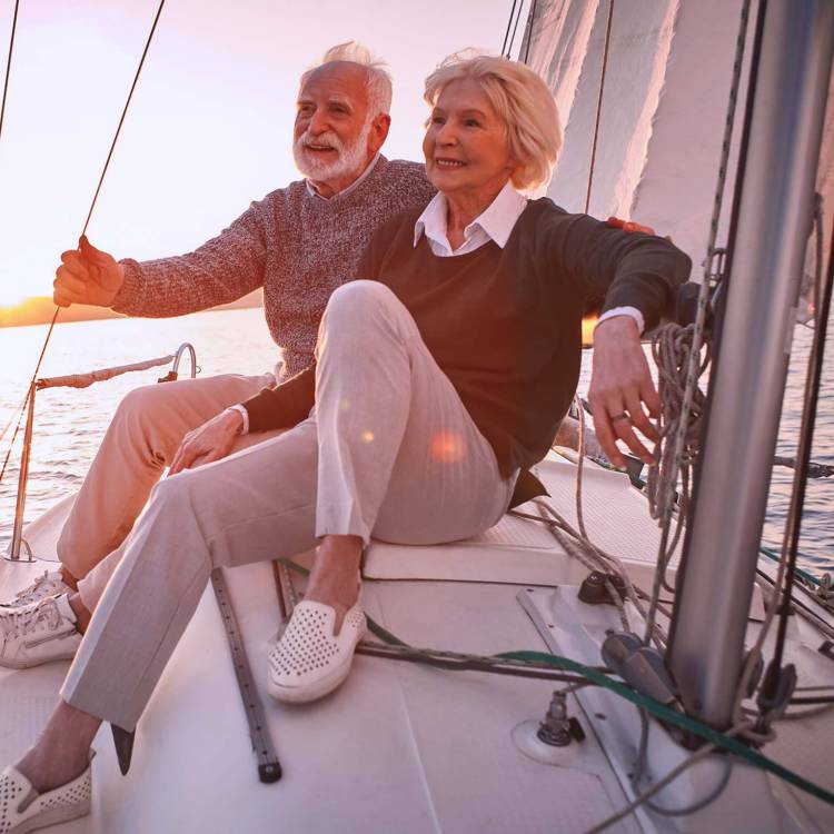Retired elderly couple happily enjoying their time on the water sitting on their yacht at sunset