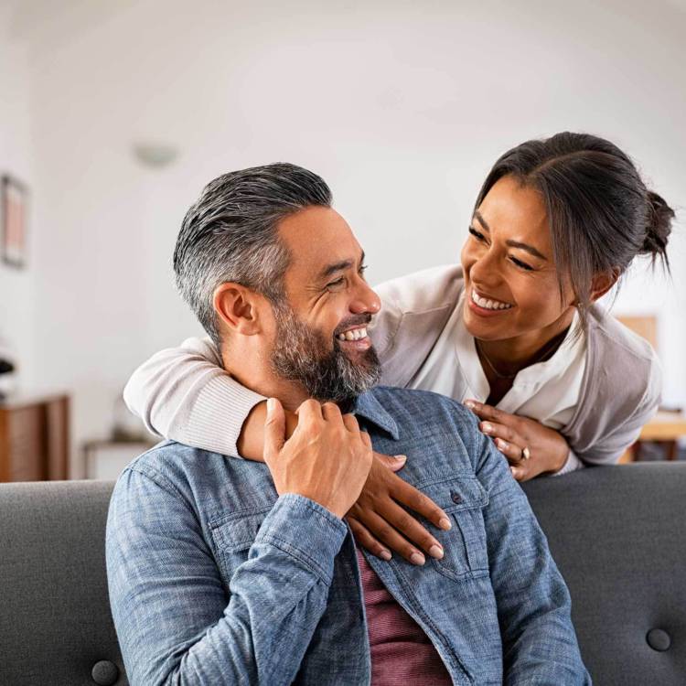 Middle ages couple hugging on a sofa in their living room and happily smiling