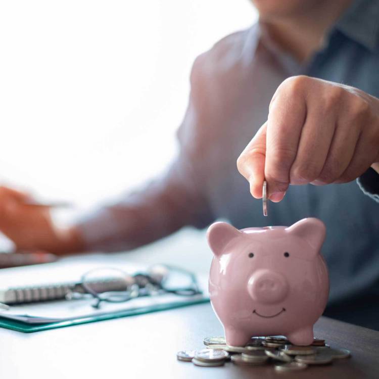 Client dropping a coin in a piggy bank while sitting at his desk