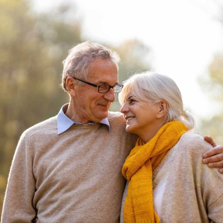 Retired elderly couple taking a walk outside enjoying the sun and smiling facing each other