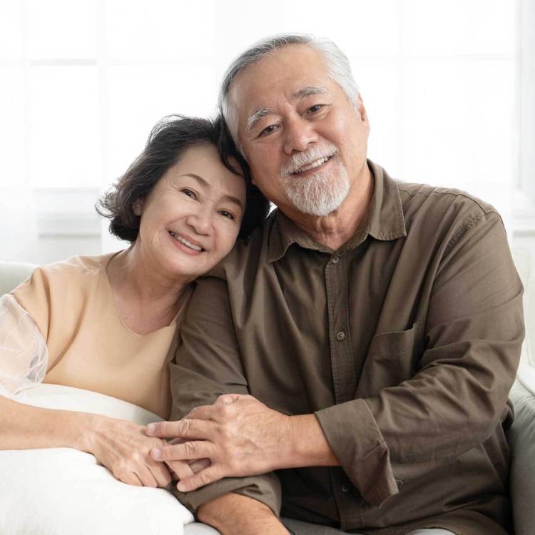Retired elderly client couple sitting happily on a sofa smiling