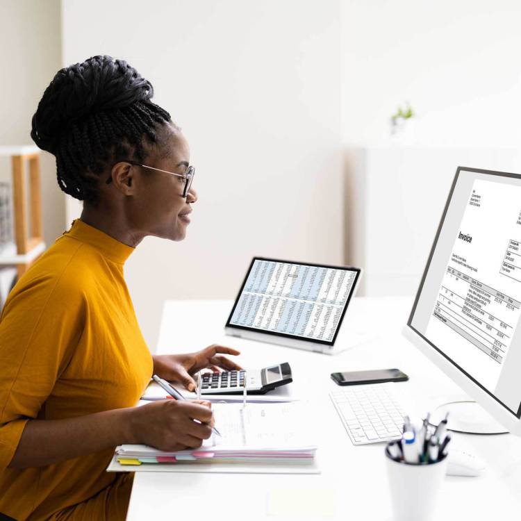 Accountant sitting at her desk looking at her desktop monitor and working with her documents and calculator