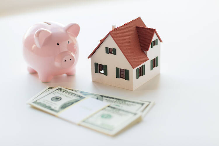 Small scale figure of a house, piggy bank and stack of cash sitting on a table