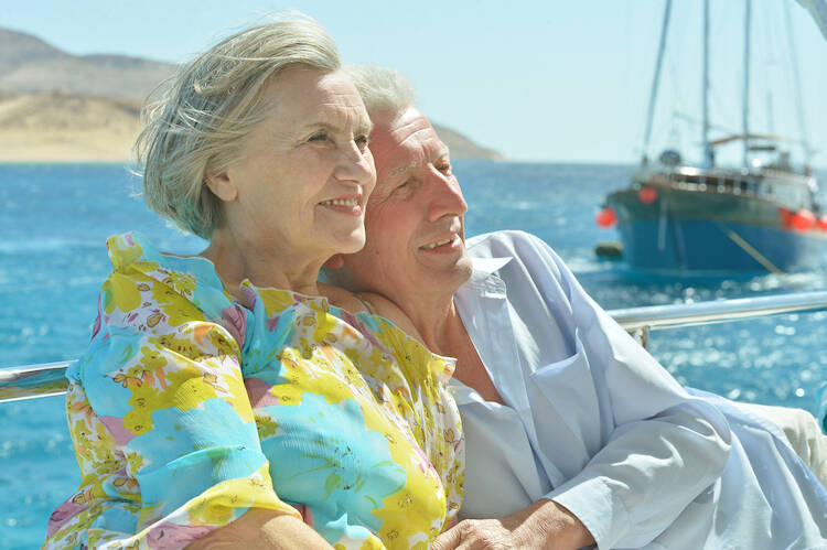 Retired elderly couple sitting outside next to the ocean enjoying the sun and boats sailing