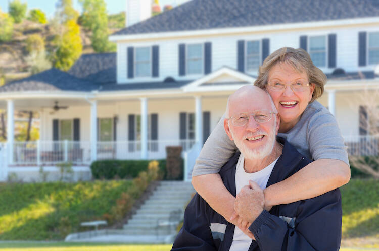 Retired elderly senior couple hugging each other happily outside in front of their home