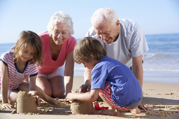 Grandparents building sandcastles on a beach with grandchildren enjoying retirement
