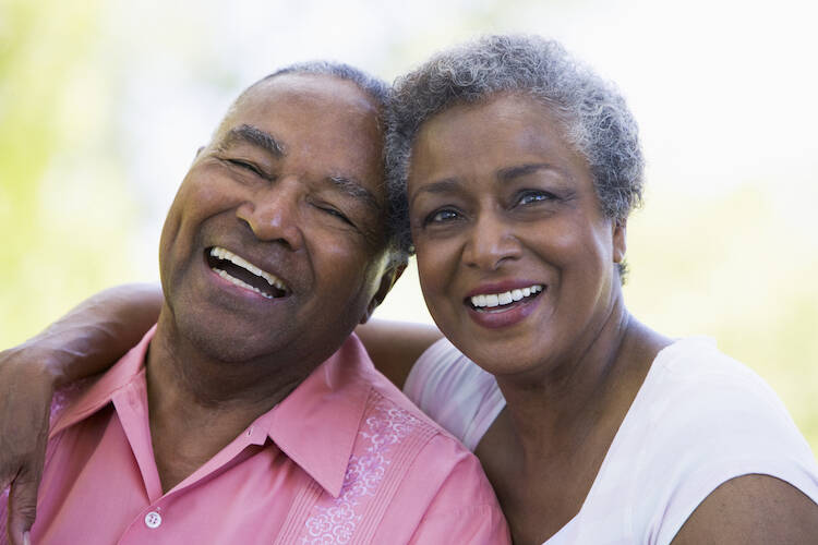 Retired elderly senior couple sitting outdoors, hugging and smiling happily