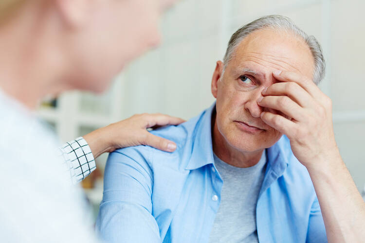 Retired elderly man looking worried with a hand to his face receiving health news from a medical professional