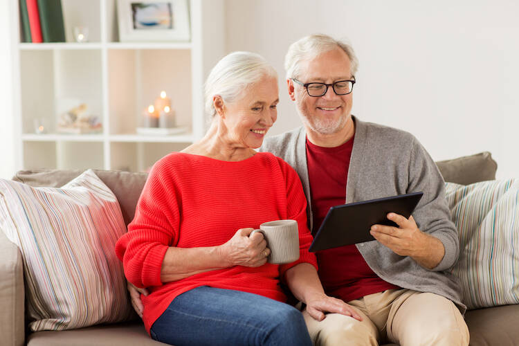 Retired elderly senior couple sitting on a sofa in their living room happily looking at a table together
