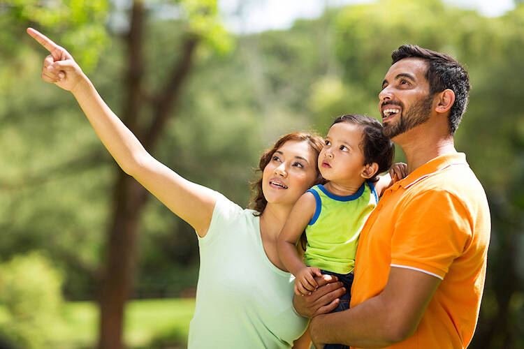 Pair of parents looking at something outside with the father holding their infant son in his arms