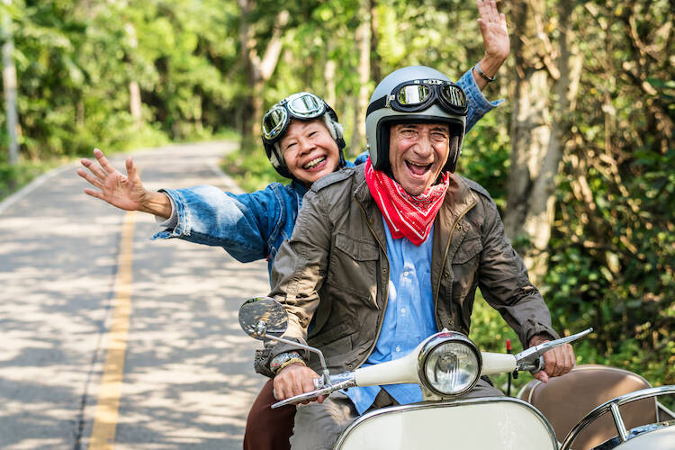Retired elderly senior couple outside riding a motorcycle together smiling happily enjoying retirement