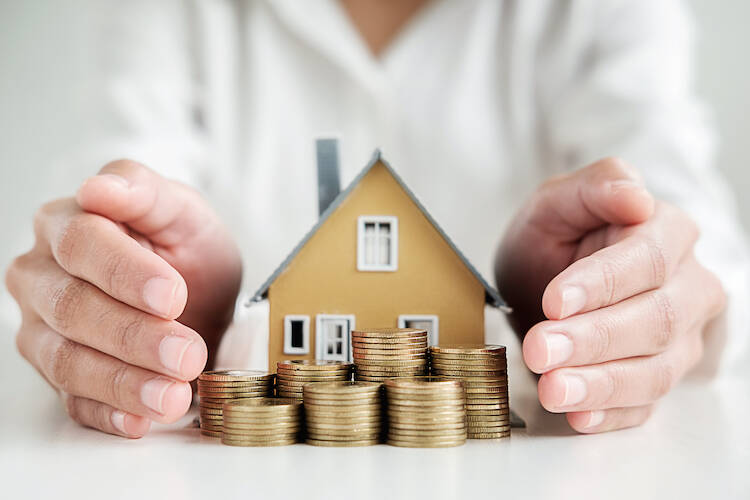 Client putting their hands around a small figured, constructed house and many piles of coins