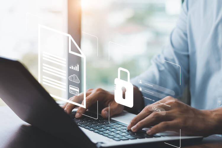 Person sitting at a table typing on a laptop with two holographic images of a lock and paper document hovering over hands